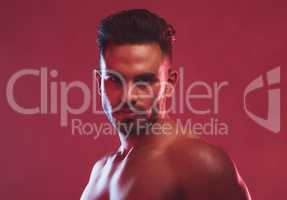 One handsome young indian man posing topless against a red studio background. Serious masculine guy looking confident and charming with muscular bare body