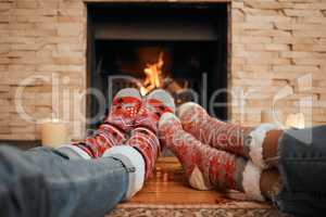 Warming up to the festive feeling. Closeup shot of a couple wearing Christmas socks while relaxing with their feet up by a fireplace at home.