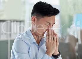One sick asian businessman blowing runny nose with tissue while working in an office. Guy feeling unwell with flu, cold and covid symptoms. Suffering with congestion, sinus and seasonal spring allergy
