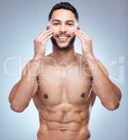 Ensuring he ages well. Shot of a handsome young man applying moisturiser to his face against a studio background.