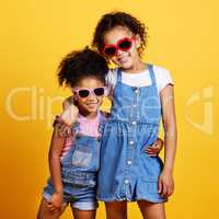 Studio portrait two mixed race girl sisters wearing funky sunglasses Isolated against a yellow background. Cute hispanic children posing inside. Happy and carefree kids imagining being fashion models