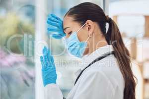Young stressed and overworked doctor wearing mask and gloves while standing at a window in a hospital or clinic. One female only looking worried, hopeless and anxious while struggling with a challenge