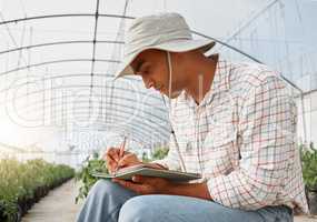 Profitability is an important business goal to plan for. a young man writing notes while working in a greenhouse on a farm.