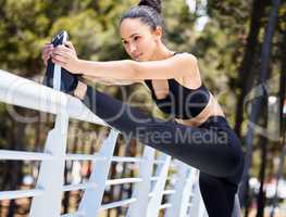 One fit young mixed race woman standing on one leg and reaching to touch foot for warmup stretches to prevent injury while exercising outdoors. Hispanic athlete staying motivated and determined while preparing for training workout or run