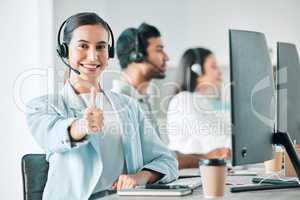 For service thats rated five stars. Portrait of a young call centre agent showing thumbs up while working in an office with her colleagues in the background.