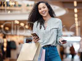 Portrait beautiful mixed race woman standing with her phone and credit card while shopping in a mall. Young hispanic woman carrying bags, spending money, looking for sales and enjoying retail therapy