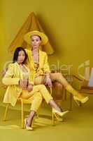 Exist bolding and brightly. Studio portrait of a two young women dressed in stylish yellow clothes against a yellow background.