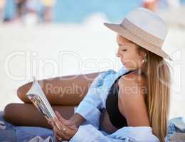 One beautiful young caucasian woman relaxing on the beach. Enjoying a summer vacation or holiday outdoors during summer. Taking time off and getting away from it all. Reading alone on the sand outside