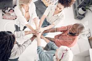 Group of five diverse businesspeople piling their hands together in an office at work. Business professionals having fun standing with their hands stacked for support and unity from above