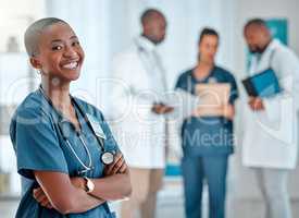 Mature african american female doctor standing with her arms crossed while working at a hospital. One expert medical professional smiling while standing at work with colleagues at a clinic