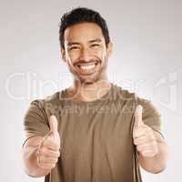 Handsome young mixed race man giving thumbs up while standing in studio isolated against a grey background. Hispanic male showing support or appreciation. Backing or endorsing a product or company