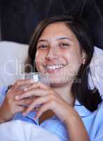 Hydration will keep you glowing. a young woman drinking a glass of water in bed at home.