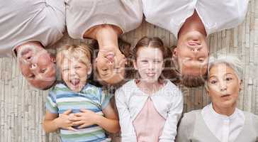 A family bonding together and being playful, showing different expressions while bonding and enjoying quality time. Above happy fun family making silly faces lying together on a living floor at home.