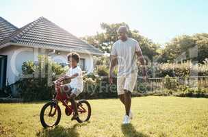 Adorable little african american boy learning to ride his bike outside with father. Dad and son having fun in their backyard on a sunny day
