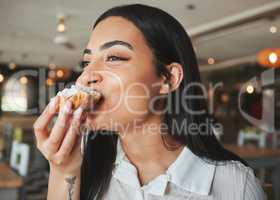 The perfect time to indulge. a beautiful young woman biting into a tasty treat in a cafe.