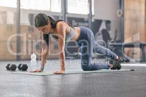 One fit young hispanic woman doing bodyweight push up exercises on one knee while exercising in a gym. Focused female athlete doing press ups to build muscle, enhance upper body, strengthen core and increase endurance during a training workout