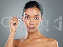 Lets jump on skincare. Shot of a beautiful young woman applying a face serum with a dropper.