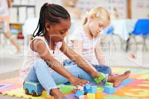 Little african american girl and classmate playing with colourful educational toy blocks on the floor at preschool or kindergarten. Kids having fun while engaged in creative learning and development