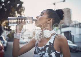 One fit young mixed race woman taking a rest break to drink water from a bottle while exercising outdoors. Female athlete quenching thirst and cooling down after running and training workout in the city