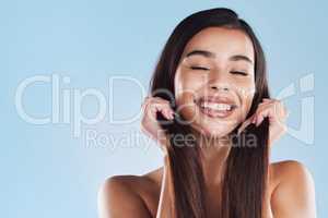 One beautiful young hispanic woman touching her sleek, silky and healthy long hair while smiling against a blue studio background. Confident and happy mixed race model with flawless complexion and natural beauty