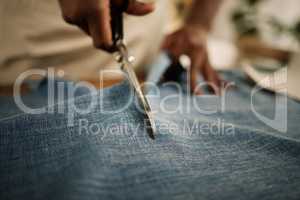 Closeup of hand of fashion designer using a scissor to cut a fabric sample. Tailor cutting a piece of denim material. Seamstress cutting into a piece of material. Entrepreneur working in a studio
