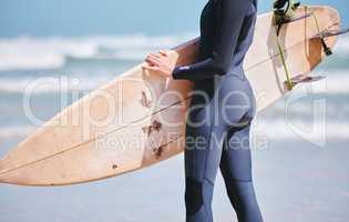 Closeup of one caucasian woman holding a surfboard and wearing wetsuit at the beach. One female only surfing as a fun hobby and exercise at sea. Active surfer from the back getting ready to ride waves