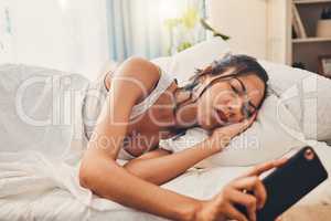 A young mixed race woman looking depressed while scrolling social media and lying in bed. An attractive Hispanic female using her cellphone and looking exhausted while resting in her bedroom