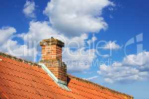 A house with a red brick chimney on an asbestos slate roof outside with a blue sky background. Exterior building designed construction and architecture of a rooftop chute for fireplace smoke and heat