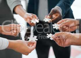 Putting the pieces together. a group of unrecognizable businesspeople holding puzzle pieces while standing in the office.