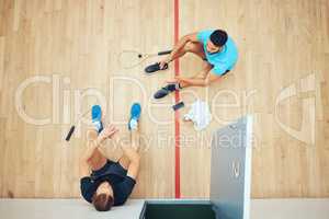 Above view of two unknown athletic squash players sitting together after playing court game. Fit active mixed race and caucasian athletes resting after training practice in sports centre. Sporty men