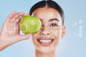 Beautiful young mixed race woman with an apple isolated in studio against a blue background. Her skincare regime keeps her fresh. For glowing skin, eat healthy. Packed with vitamins and nutrients