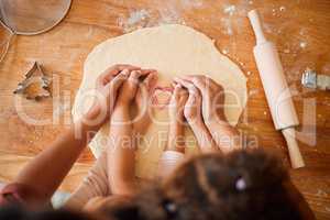 An unknown mother and daughter bonding while baking cookies in a kitchen at home. Unrecognizable mixed race family of two having fun while making shapes in dough