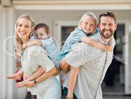 Portrait of happy parents giving their little children piggyback rides outside in a garden. Smiling caucasian couple bonding with their adorable son and daughter in the backyard. Playful kids enjoying
