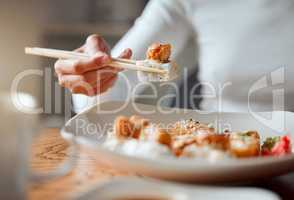 Closeup of woman eating plate of sushi with chopsticks. Hand of a woman enjoying a meal at home. Woman enjoying asian food at home. Delicious sushi is always a great meal. Woman eating seafood