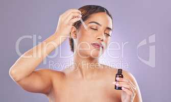 Get your glow on. a young woman applying a serum to her face against a pink background.