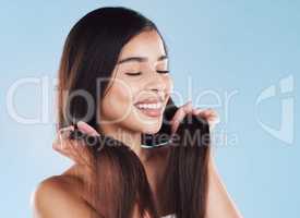 One beautiful young hispanic woman touching her sleek, silky and healthy long hair while smiling against a blue studio background. Confident and happy mixed race model with flawless complexion and natural beauty