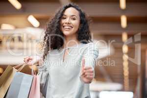 Portrait beautiful mixed race woman giving thumbs up and standing in a mall while shopping. Young hispanic woman carrying bags, spending money, looking for sales and enjoying her retail therapy