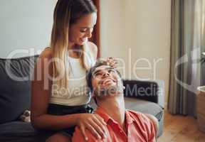 Loving young caucasian couple sitting together at home spending time and happy to be together. Happy young woman sitting on couch while her boyfriend sits between her legs as she plays with his hair. Woman gently massages boyfriends head to relax