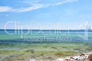 Landscape view of a blue ocean with clear skies on the horizon on a warm summer day. Little waves crash on a quiet calm rocky shore in the mediterranean sea. Panoramic coastline location for tourist