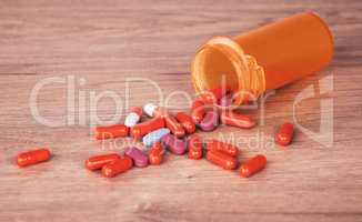 An open orange bottle of brightly coloured pills spilled onto a wooden table. Vitamin supplements are a good way to stay healthy. Chronic and prescription medication is usually covered by medical aid