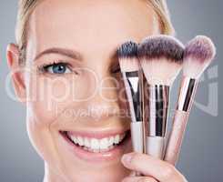 Theres nothing wrong with a little appearance enhancement. Studio portrait of an attractive mature woman holding a collection of makeup brushes against a grey background.