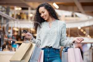 One beautiful mixed race woman holding a credit card and standing in a mall shopping. Young hispanic woman carrying bags, spending money, looking for sales and getting in some good retail therapy