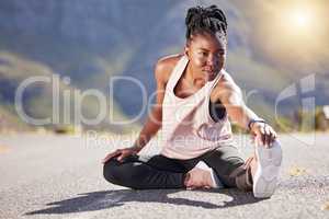 Active african american woman sitting and stretching her legs before running on a road. Female runner warming up her body before a run or jog