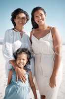 Smiling mixed race family standing together on a beach. Happy hispanic grandmother bonding with granddaughter over a weekend. Adorable little girl enjoying free time with single mother and parent