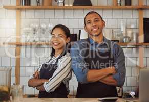 Business partners standing back to back in their coffeeshop. Restaurant colleagues standing next to each other. Portrait of two entrepreneurs arms crossed. Businesspeople in their cafe kitchen