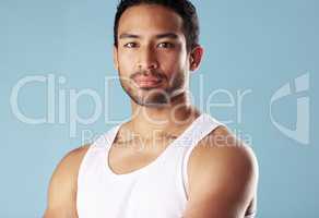 Handsome young hispanic man posing in studio isolated against a blue background. Mixed race male athlete wearing a vest and looking confident, healthy and fit. Exercising to increase his strength