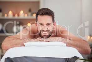 Portrait handsome caucasian man lying on a table at the spa for his back massage. Shirtless man relaxing in a day spa ready to be pampered. Handsome customer smiling while under a towel