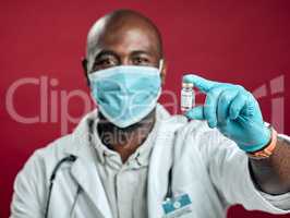 African american covid doctor holding corona vaccine while wearing surgical face mask. Closeup portrait of black physician with drug vial against red studio background with copyspace. Virus protected