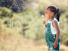 Happy little african american girl blowing dandelion flower outside. One cheerful black child having fun playing at the park during spring on a sunny day. Allergy free concept