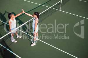 Ending off their friendly match on a high note. two sporty young women giving each other a high five while playing tennis together on a court.